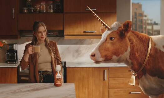 A horned cow enters the kitchen as a woman enjoys her Natural Bliss drink