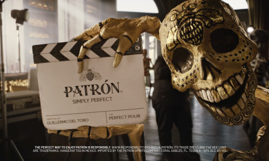 A screenshot of PATRÓN's "The Perfect Pour" campaign showing a Mexican-styled skeleton holding a branded sign