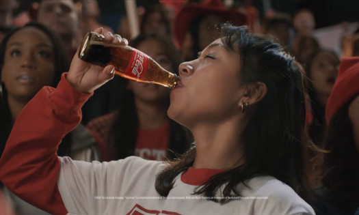 A girl drinking a bottle of Coca-Cola in a sports crowd