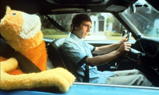 A man drives with a puppet in the passenger seat