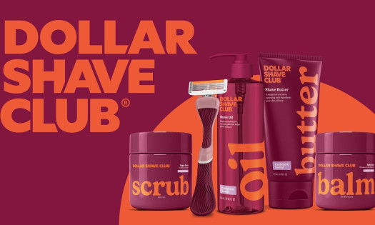 Dollar Shave Club women’s grooming line featuring razor, shave oil, butter, scrub, and balm in bold maroon and orange packaging against a branded background.