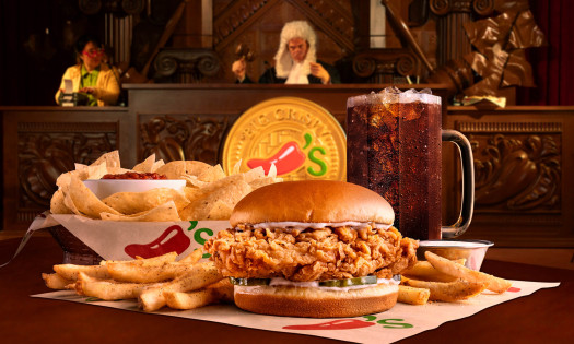 Big Crispy chicken sandwich meal with fries, chips and salsa, and a drink displayed in a courtroom setting, representing Chili's "Food Court" pop-up where fast food is put on trial.