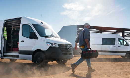 Mercedes-Benz Sprinter carrying the gear of a worker walking with his tool bag to a worksite. Another Sprinter is in the background.