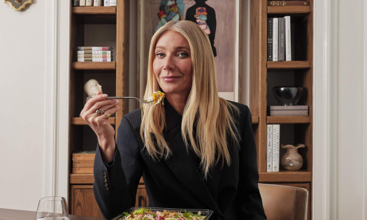 Gwyneth Paltrow is about to take a bite of a goop kitchen salad. A glass of water and salad dressing is on the side.