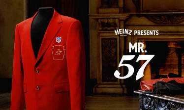 Red blazer displayed on a mannequin featuring an NFL patch and "Mr. 57" crest, set in a formal interior with a fireplace, alongside the text "Heinz Presents Mr. 57."