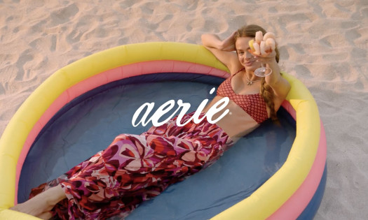 A screenshot from Aerie's summer campaign showing a girl lying in an inflatable pool holding up a cocktail glass