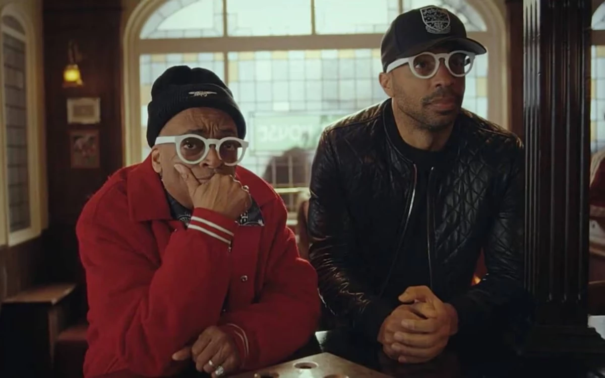 Spike Lee and Thierry Henry staring off camera seated at a bar.