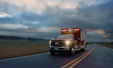 Ford ambulance drives down a rural road in the "Born In A Ford" campaign about emergency births and first responders.