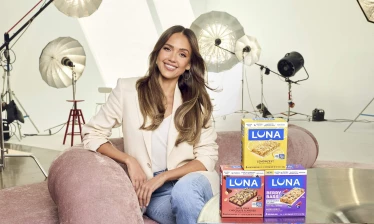 Jessica Alba pictured with LUNA Bar product boxes with photoshoot equipment in the background.