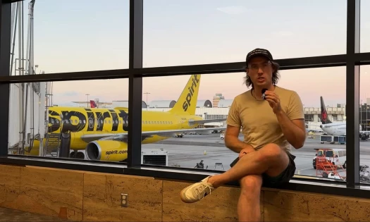 Hunter Peterson holding a mic sitting beside a window showing a Spirit Airlines plane