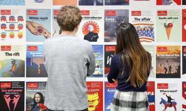 Two people standing in front of a wall displaying The Economist magazine covers.Two people standing in front of a wall displaying The Economist magazine covers.