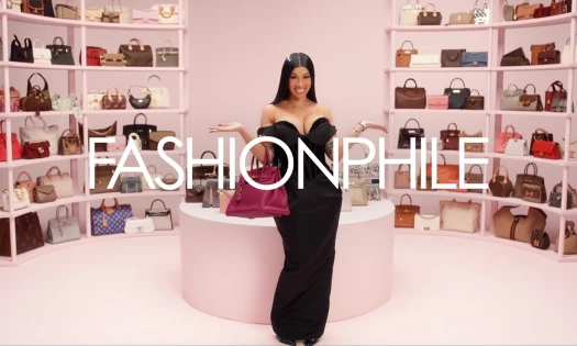 Cardi B stands in a pink handbag showroom holding a luxury bag in Fashionphile’s “Get Your Bag” campaign.