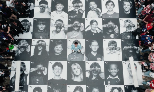 Overhead view of a PUMA fan installation showing black-and-white portraits of supporters holding tattoo sleeves over their eyes, with Christian Pulisic standing at the center.