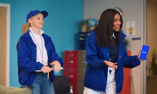 Elizabeth Banks and Gabrielle Union in coaches uniforms, Union holding a phone with the Paze load screen visible