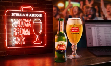 Stella Artois “Work From Bar” campaign visual showing a neon WFB sign, a Stella Artois 0.0 bottle, a chalice, and a laptop on a bar during a soccer match.
