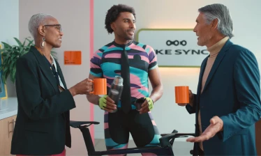 A man in cycling attire talks to two people in the office