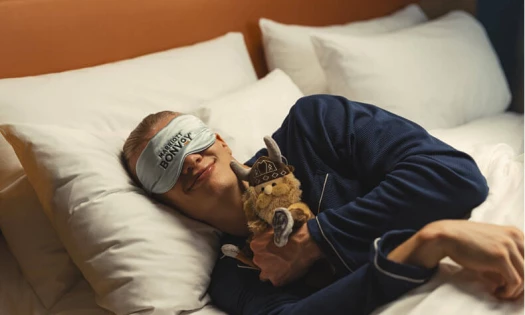 Erling Haaland lies in a hotel bed wearing a Marriott Bonvoy sleep mask and holding a plush mascot.