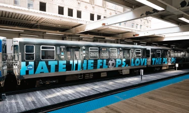 A DUDE Wipes-wrapped train sits at a Chicago station with “Hate the Plops” displayed across its side.