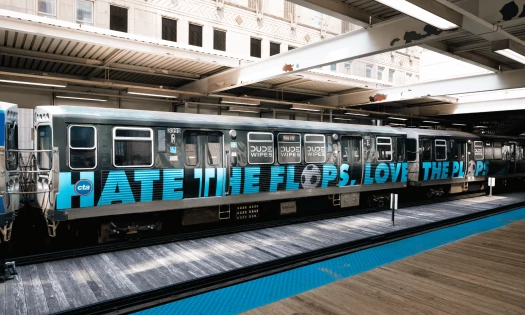 A DUDE Wipes-wrapped train sits at a Chicago station with “Hate the Plops” displayed across its side.