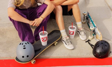 Aerial shot of skaters sitting on the sidewalk with their boards, helmets, and QuikTrip branded drinks around them.