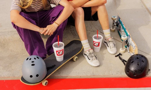 Aerial shot of skaters sitting on the sidewalk with their boards, helmets, and QuikTrip branded drinks around them.