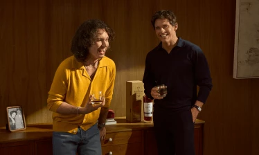 James and Jack Marsden hold whisky glasses beside a bottle and box of The Macallan Sherry Oak 30 in a warm wood-paneled room.