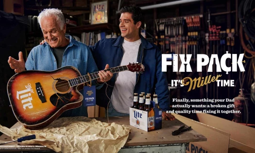 A father and son repairing a guitar with a six pack of Miller Lite on the work bench.