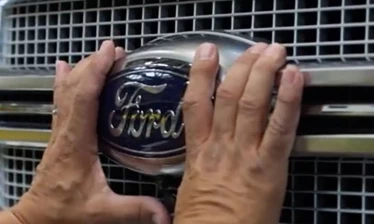 A person fitting a Ford logo emblem onto a vehicle.