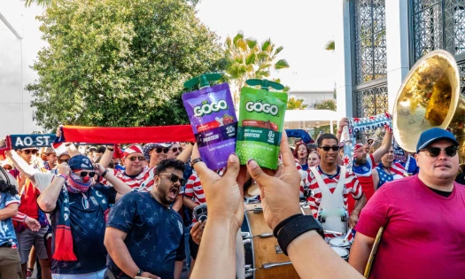 A person holds up two GOGO SqueeZ pouches in from of U.S. soccer fans.