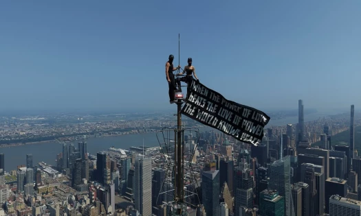 A masked couple on top of the Empire State Building's spire with a black banner.