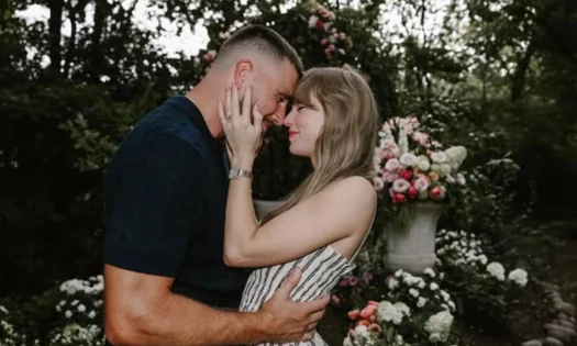 Travis Kelce and Taylor Swift embracing in a floral garden.