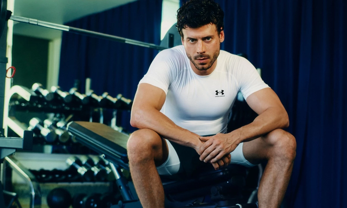 'Heated Rivalry' Star François Arnaud sitting down on a bench press wearing Under Armour