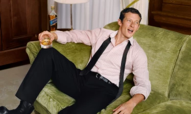 Callum Turner with a glass of Johnnie Walker, sitting on a green couch