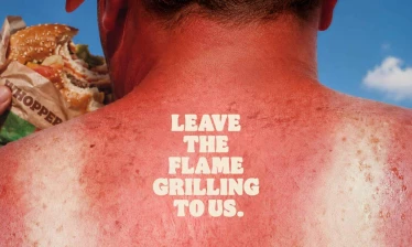 The back of the neck of an aggressively sun burnt man with a shirt outline. He is eating a Burger King Whopper and the tagline: Leave The Flame Grilling To Us" sits the middle of his back.