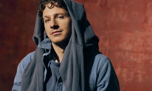 Charlie Puth wearing a blue jacket as he sits on the floor