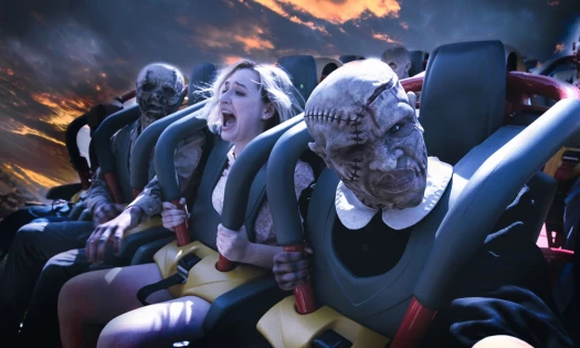 A person on a rollercoaster and seated between two Halloween monsters.