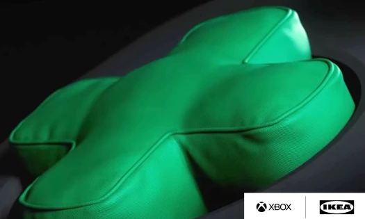A green cushion shaped like an Xbox D-pad with the IKEA and Xbox logo in the bottom right corner.