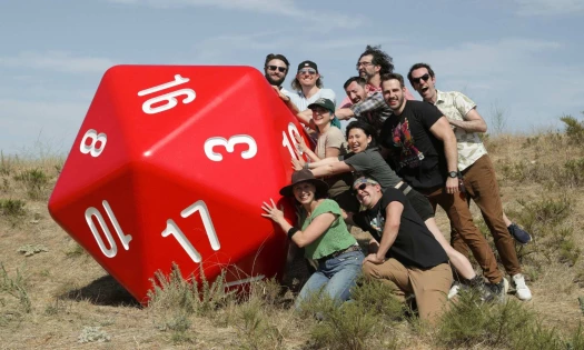 Ten creators pose next to a red, six-foot D20 die in the wilderness.