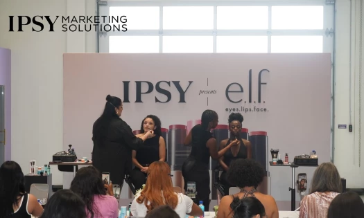 IPSY presents e.l.f. at a beauty activation where make-up artists are giving a tutorial to attendees. IPSY Marketing Solution logo is in the top left corner.