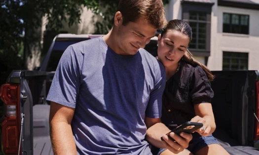 NFL quarterback Drake Maye and content creator Ann Michael Maye sitting on the back of a truck scrolling on a phone.