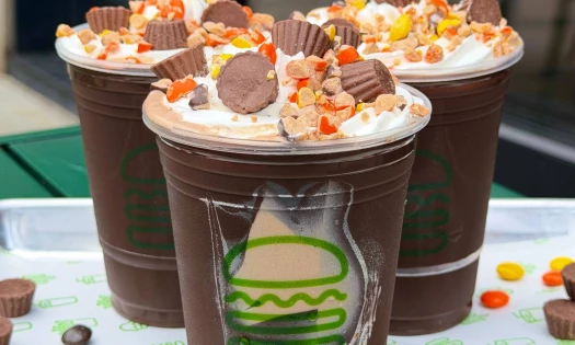 Three Shake Shack's Reese's Peanut Butter Cup Shake on a tray with scattered Reese's candies.