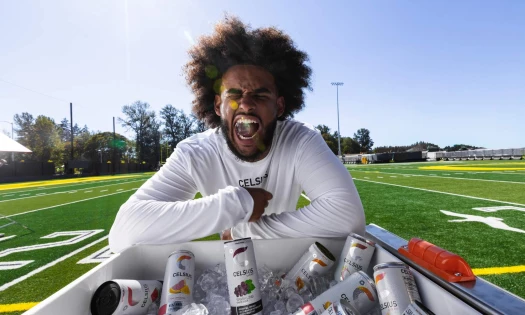 Oregon quarterback Dante Moore biting on a block of ice behind a ice box of CELSIUS Energy Drinks.