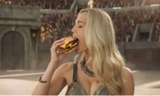 A woman eating a Carl's Jr. buger inside a colosseum