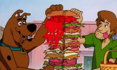 A tall sandwich being sliced in half by Scooby and Shaggy