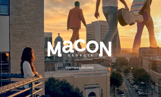 A woman on a balcon watches three larger-than-life figure walk through Macon, Georgia.