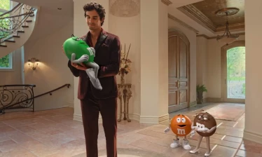 A man cradling an M&M's spokescandy while others look