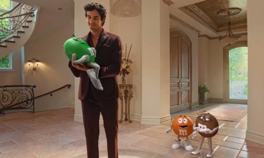 A man cradling an M&M's spokescandy while others look