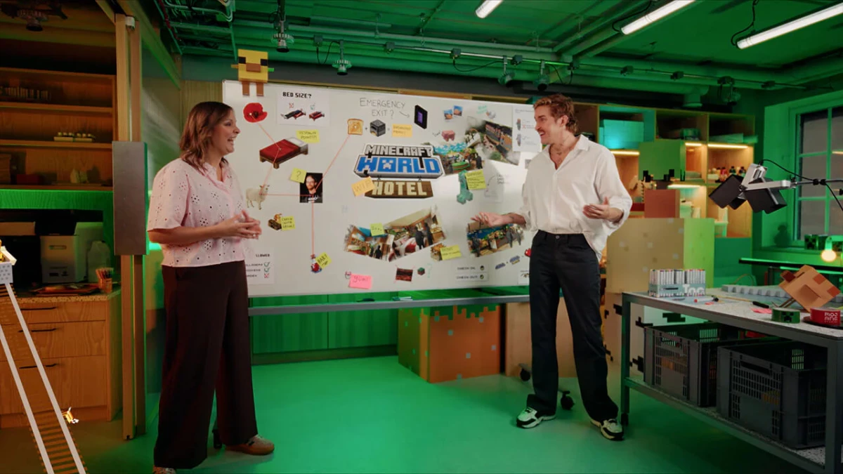 Two people stand in front of a whiteboard displaying the new Minecraft World Hotel concept