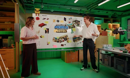 Two people stand in front of a whiteboard displaying the new Minecraft World Hotel concept
