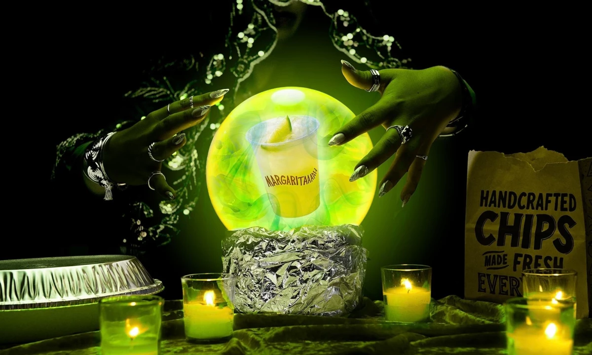 A Chipotle margarita in a crystal ball in foil, surrounded by candles, a bag of chips, and a pair of hands.